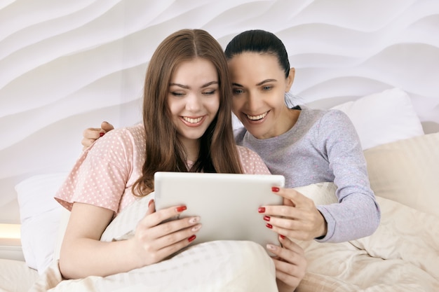 タブレットPCのメッセンジャーを介したビデオ通信の母と娘は、インターネットを介して誰かと通信し、笑顔を見せる