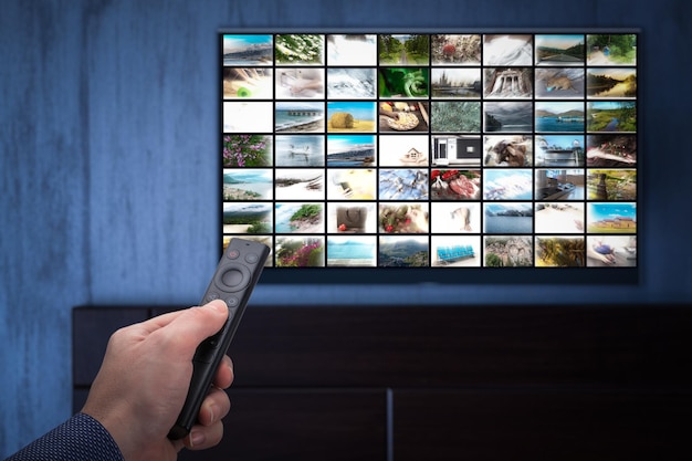 Video on demand service on smart TV. man choosing what to watch on TV at home. Video on demand or VOD. Online movie stream service in smart tv. Male hand holding TV remote control.