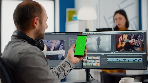 Video editor talking on video call holding smartphone with green screen