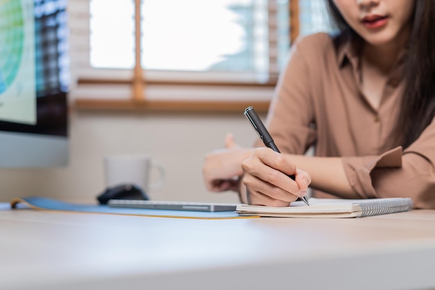 Video meeting conference via camera Beautiful asian young business woman hand in writing making notes by pen using PC computer sitting in home office freelancer workingTechnology social distance