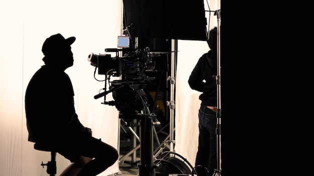 Video production behind the scenes which film crew team in silhouette shooting or recording tv movie commercial with professional equipment such as high definition camera with monitor in studio set.