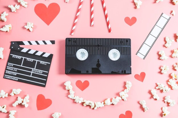 Videoband clapperboard papieren hart filmstrip rietjes en een popcornglimlach op een roze achtergrond