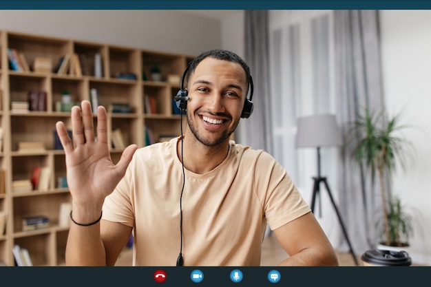 写真 カメラと手を振ってweb会議を持っているヘッドセットの陽気なアラブ人のビデオコールのスクリーンショット