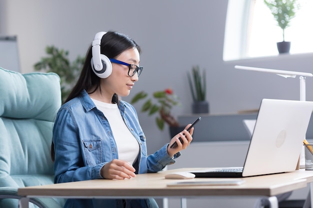 Videochat met vrienden, jonge mooie aziatische vrouw die een koptelefoon draagt met een telefoon in haar hand