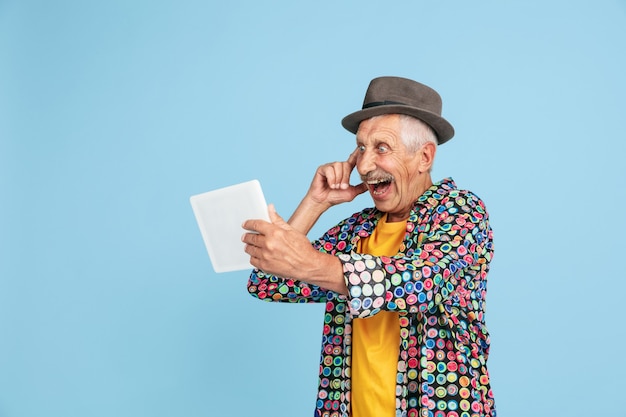 Videochat using tablet shocked Portrait of senior hipster man in stylish hat on blue