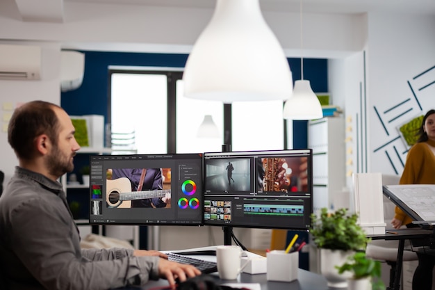 Videograaf bewerken, beeldmateriaal en geluid knippen op de computer met dubbele monitoren die werken in het kantoor van een creatief bureau