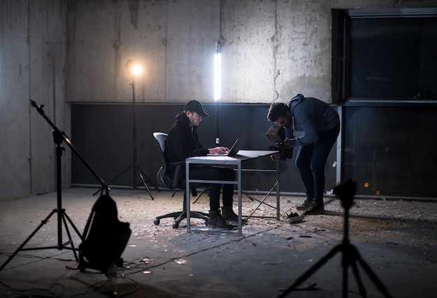 videograaf die jonge getalenteerde hacker opneemt terwijl hij op een laptop in een donker kantoor werkt met een betonnen muur op de achtergrond