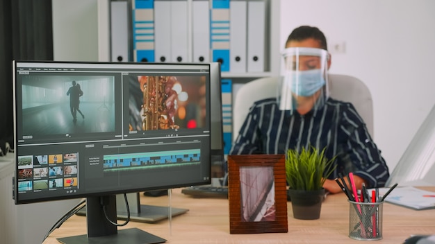 コンテンツを作成するビデオプロジェクトで働く保護マスクを持ったビデオグラファー、新しい通常のオフィススタジオに座っているブロガーのチーム。ビデオdurigの世界的大流行を編集するフリーランサー
