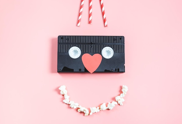 Videotape paper heart straws and a popcorn smile on a pink background