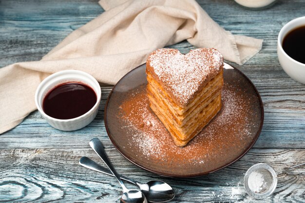 Waffle viennesi a forma di cuore con zucchero a velo, vaniglia e cacao su fondo in legno grigio.