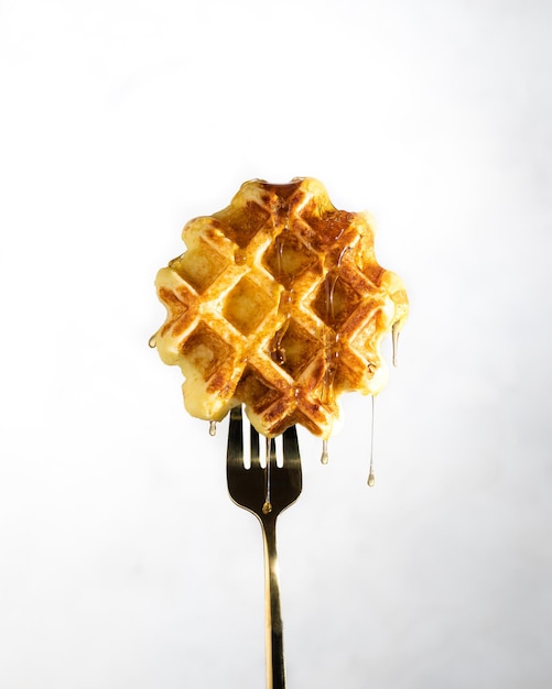 Viennese waffle with honey drops on a fork on a white background isolate