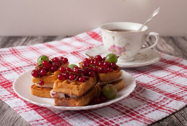 Viennese waffles with berries and a cup of tea stand on a checkered tablecloth on the table