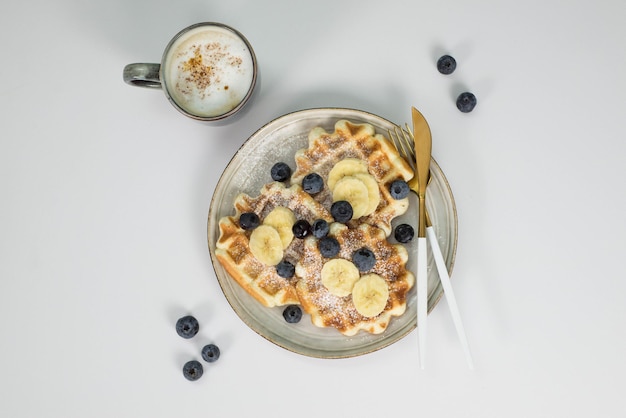 Viennese waffles with blueberries and banana on a light plate on a light background