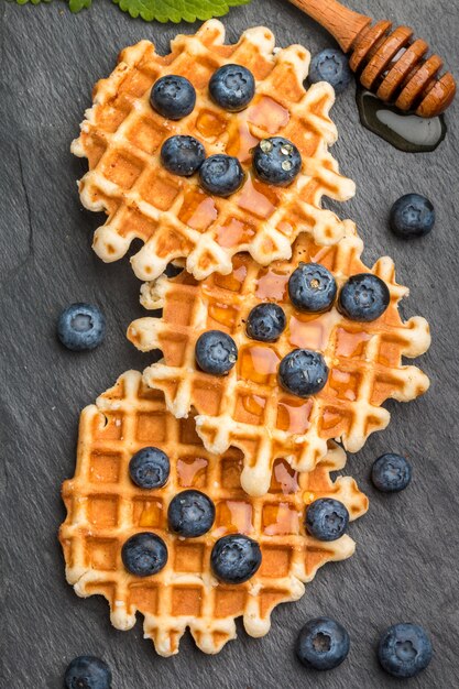 Viennese waffles with honey and fresh berries blueberry and mint on black surface, Delicious dessert