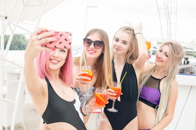 Vier aantrekkelijke meisjes die op de strandbar rusten, drinken een verfrissende cocktail, lachend en plezier makend De heldere badpakken en zonnebril