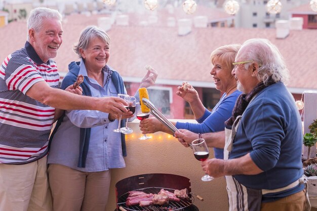 Vier actieve senioren gepensioneerd veel plezier op het terras thuis koken wat bbq iedereen lacht en blijf in vriendschap bij elkaar op een mooie zonnige dag. vakantie en relatie mensen concept