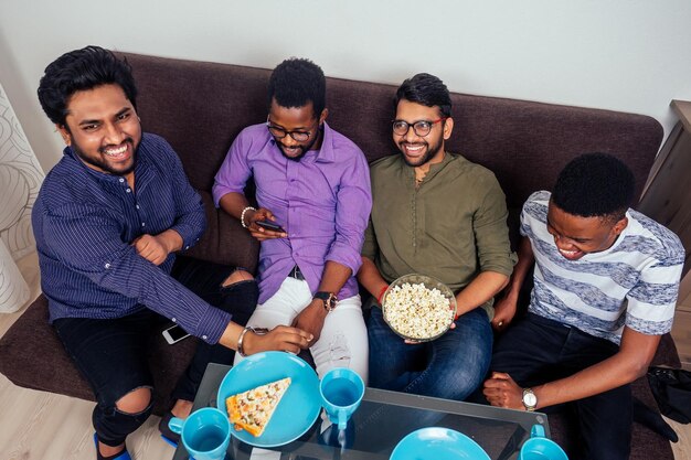 Vier Afro-Amerikaanse mannen eten pizza thuis en gooien popcorn in elkaar