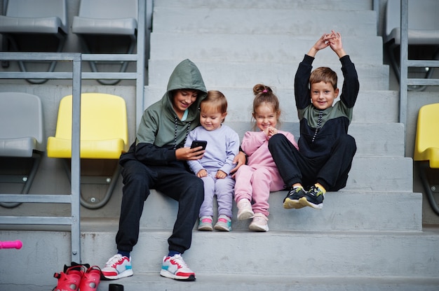 Vier cuttie kinderen zitten op sportgebied en kijken naar mobiele telefoon.