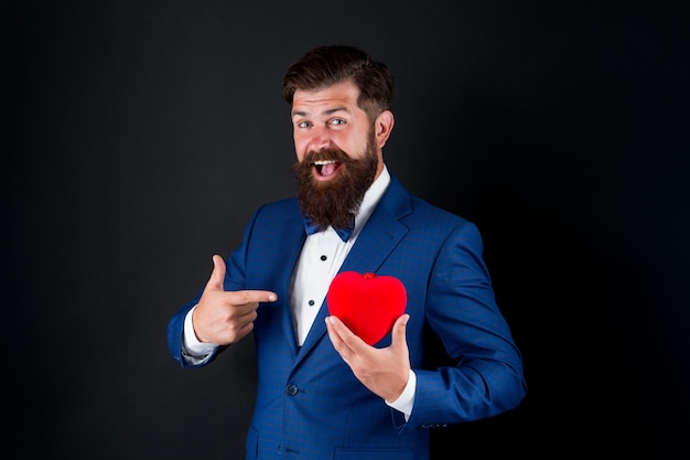 Vier de liefde. Geloof me. Fijne Valentijnsdag. Tuxedo man houdt rood hart vast. Liefdesconcept. Gepassioneerde volwassen minnaar hipster in formeel pak. Zakenman met vlinderdas. Romantische groet. Verliefd worden.