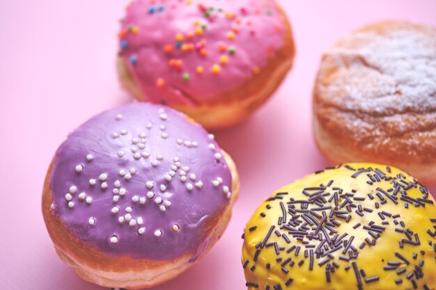 Vier donuts met gekleurd glazuur op een roze papieren achtergrond.