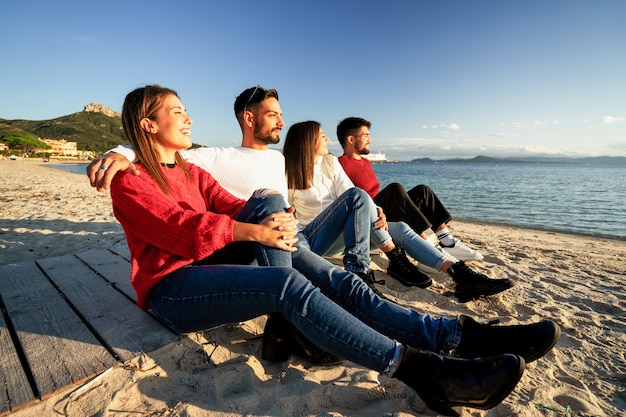 Vier duizendjarige vrienden die op een promenade van een strand in een badplaats zitten te kijken naar de ondergaande zon