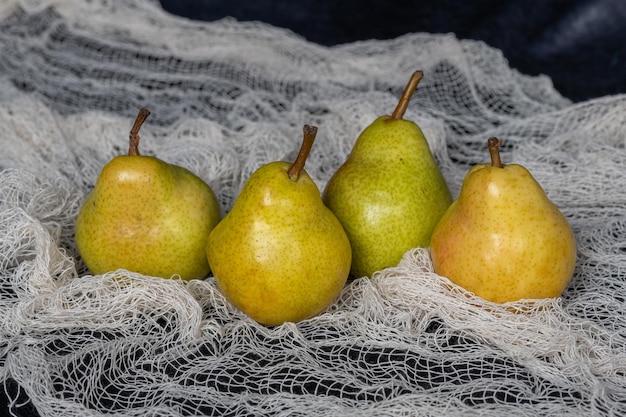 Foto vier gele en groene peren op decoratieve stof. stilleven