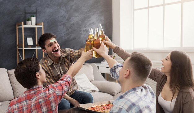 Vier gelukkige vrienden die bierflesjes rammelen terwijl ze thuis plezier hebben