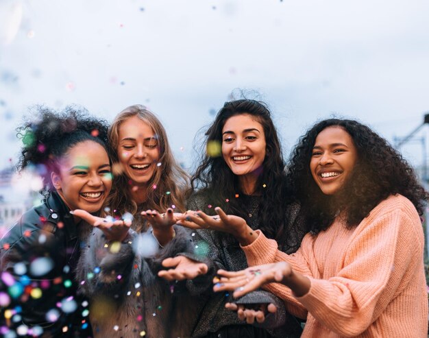 Vier gelukkige vrouwtjes gooien confetti buiten in de avond