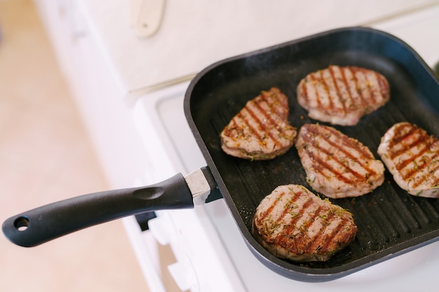 Vier geroosterde steaks op een grillpan met fijngehakte rozemarijn