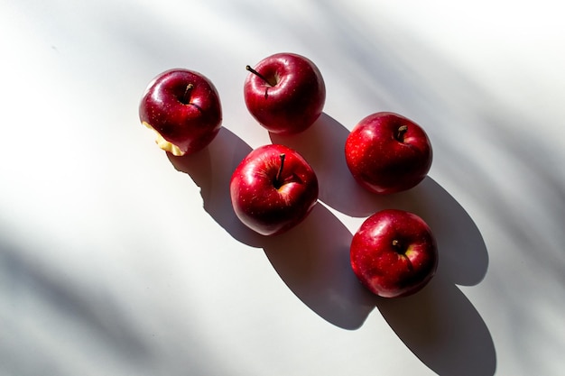 Vier hele en een gebeten rode appels op een witte tafel.