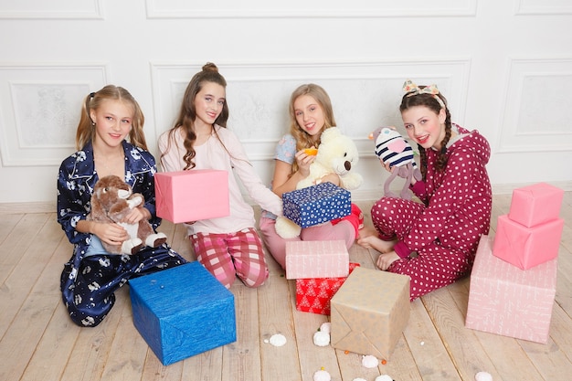 Foto vier jonge meisjes in pyjama die wachten om hun geschenkdoos te openen