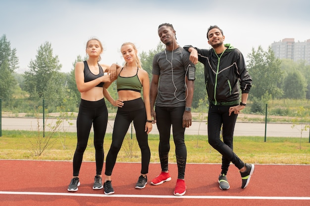 Vier jonge vriendelijke interculturele mensen in sportkleding staande op circuit van buitenstadion in stedelijke omgeving