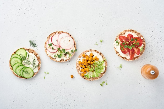 vier krokante boekweitbroodjes met roomkaas, radijs, tomaat, kikkererwten, komkommer en microgreen