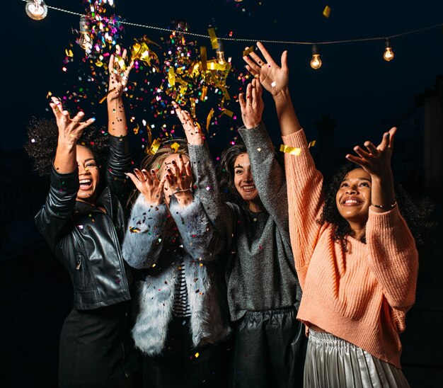 Vier lachende vrouwtjes gooien confetti in de lucht's nachts, verschillende vrouwen vieren samen.