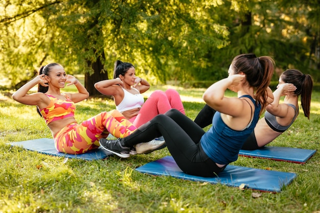 Vier mooie gemotiveerde vriendinnen doen sit-up in het stadspark.