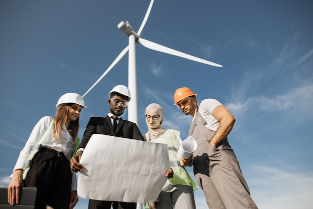 Vier partners in helmen die de blauwdrukken van windturbines bestuderen