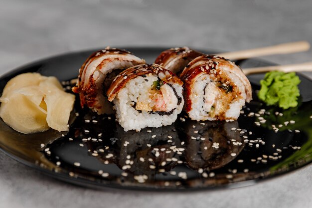 Vier porties garnalen en palingsushi met vossabisaus en gember op een zwarte plaat. Zijaanzicht