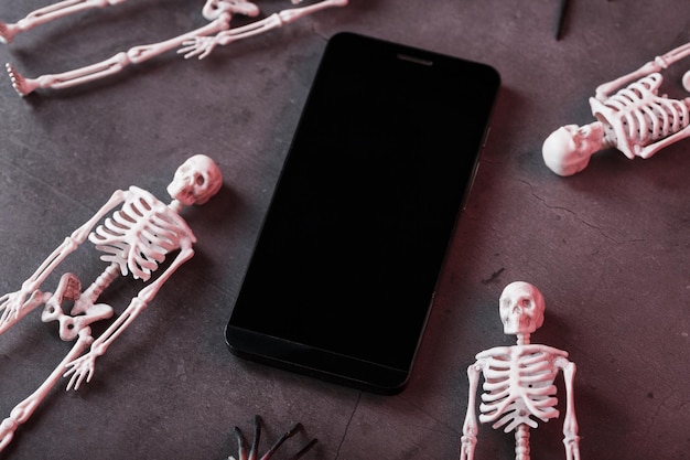 Vier skeletten liggen in de buurt van de smartphone op een donkere achtergrond. Halloween-decoratie, Bovenaanzicht, Vrije ruimte