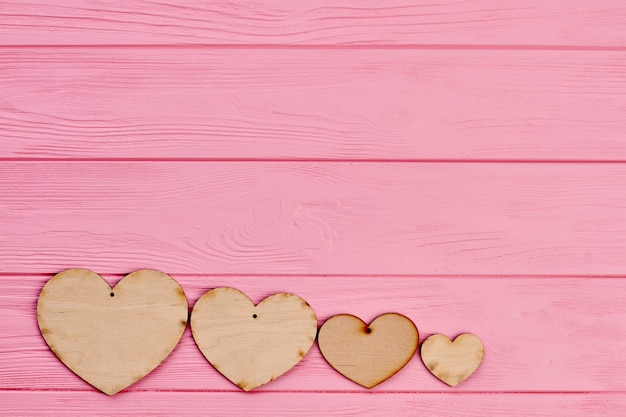 Vier triplexharten op kleurrijke achtergrond. rij van houten harten op roze houten achtergrond met kopie ruimte. valentijnsdag wenskaart.