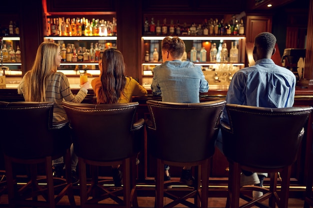 Vier vrienden drinken bier aan het loket in de bar, achteraanzicht. Groep mensen ontspannen in pub, nachtlevensstijl, vriendschap, evenementviering