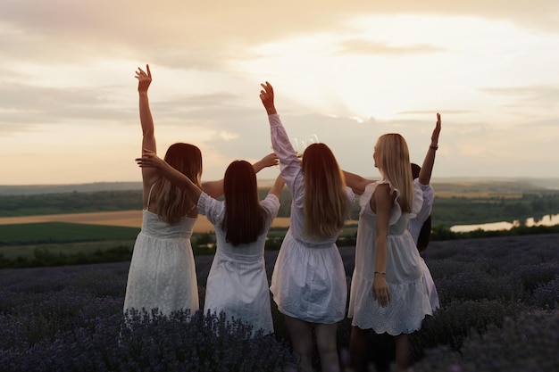 Vier vrouwen in witte jurken staan in een lavendelveld, een van hen draagt een witte jurk en de ander een witte jurk.