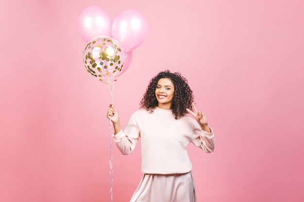 Viering concept - close-up portret van gelukkige vrolijke jonge mooie Afro-Amerikaanse vrouw met roze t-shirt met kleurrijke partij ballonnen. Geïsoleerdt tegen roze studioachtergrond.