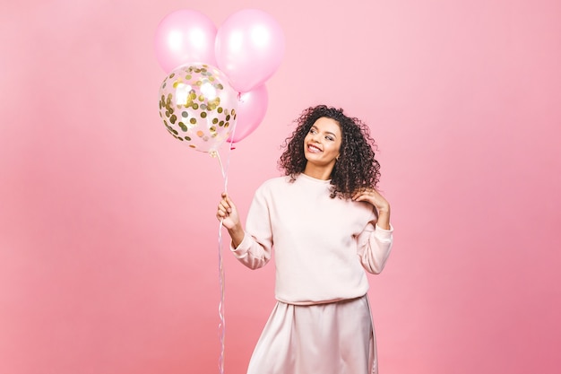 Viering concept - close-up portret van gelukkige vrolijke jonge mooie Afro-Amerikaanse vrouw met roze t-shirt met kleurrijke partij ballonnen. Geïsoleerdt tegen roze studioachtergrond.