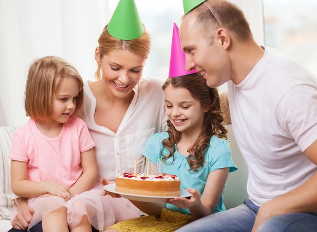 viering, familie, vakantie en verjaardagsconcept - gelukkig gezin met twee kinderen in hoeden met cake thuis