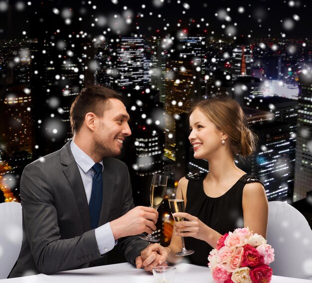 viering, Kerstmis, vakantie en mensen concept - glimlachend paar rammelende glazen mousserende wijn in restaurant over besneeuwde nacht stad achtergrond