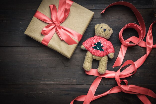 Vierkante doos verpakt in bruin kraftpapier en gebonden met rood zijden lint op bruine houten tafel met teddybeer