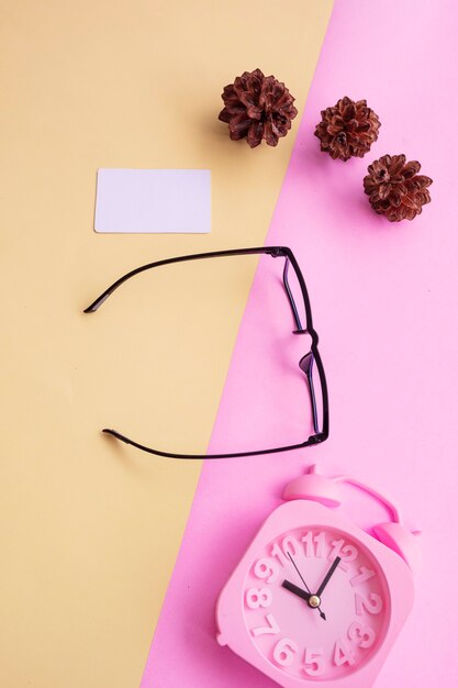 Vierkante glazen op een roze en gele achtergrond met extra accessoires een wekker en dennenboombloemen. minimale zomerstijl