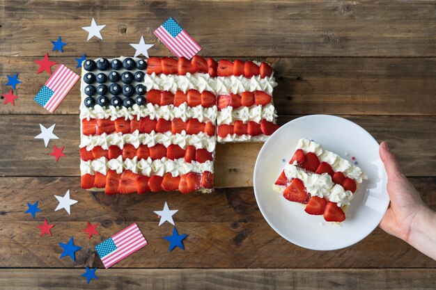 Vierkante taart met de kleuren van de Amerikaanse vlag op een houten ondergrond met decoratie Hand met bord met plakje cake Onafhankelijkheidsdag viering