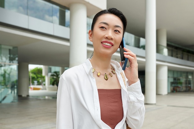Vietnamese businesswoman standing in front of office building and talking on phone