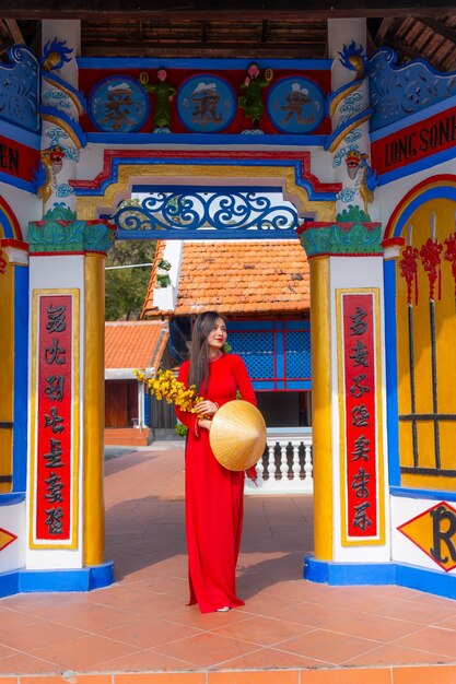 Vietnamese girl with Ao Dai dress standing in traditional house of Vietnam Text in photo mean best wishes to family happiness prosperity health Tet holiday and New Year
